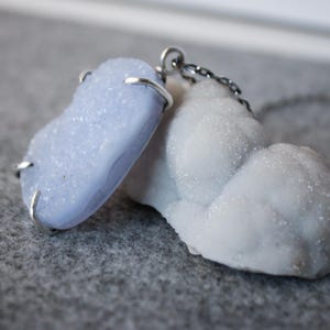 May include: A silver chain necklace with a light blue agate pendant and a white agate pendant.