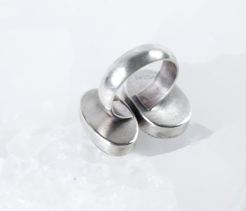 May include: Silver ring with two oval-shaped stones. The ring is marked "925" on the inside of the band.
