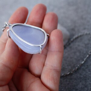 May include: A silver pendant with a light blue, irregularly shaped gemstone. The pendant is on a silver chain.