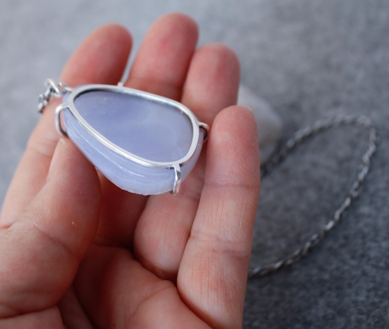 May include: A silver pendant with a light blue, irregularly shaped gemstone. The pendant is on a silver chain.