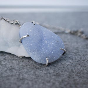 May include: A silver chain necklace with a light blue, sparkly, teardrop-shaped stone pendant.