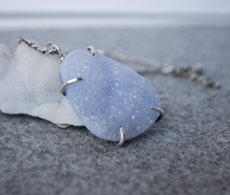 May include: A silver chain necklace with a light blue, sparkly, teardrop-shaped stone pendant.
