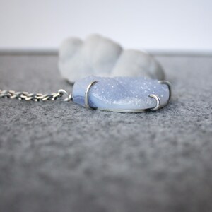 May include: A silver chain necklace with a light blue agate pendant. The pendant is set in silver and has a rough, textured surface.
