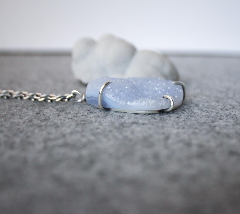 May include: A silver chain necklace with a light blue agate pendant. The pendant is set in silver and has a rough, textured surface.