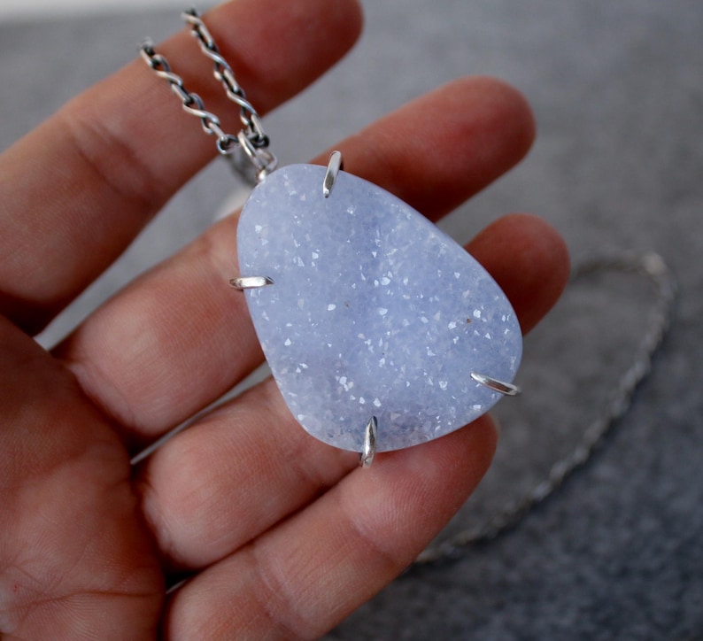 May include: A silver chain necklace with a large, light blue, irregularly shaped agate pendant. The pendant is set in a silver bezel and has a sparkly, crystalline texture.