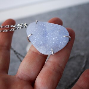 May include: A silver chain necklace with a light blue agate pendant. The pendant is a freeform shape and has a sparkly, crystalline texture.