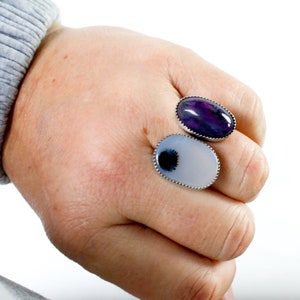 May include: Two oval-shaped rings with silver settings and agate stones. The top ring has a purple and white agate stone. The bottom ring has a white agate stone with a black and white pattern.