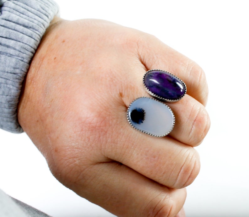May include: Two oval-shaped rings with silver settings and agate stones. The top ring has a purple and white agate stone. The bottom ring has a white agate stone with a black and white pattern.