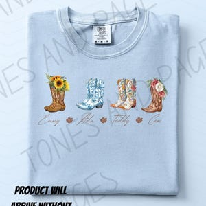 Puede incluir: Camiseta azul claro con cuatro botas de vaquero de acuarela con dise&ntilde;os florales y de girasoles. Cada bota tiene un nombre debajo: Emmy, Aida, Teddy y Cam. La camiseta tiene una etiqueta Comfort Colors.