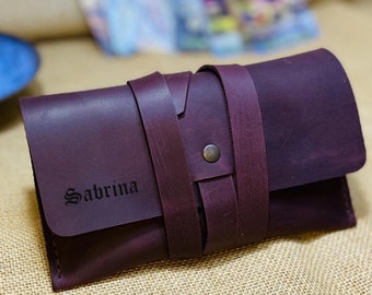 May include: A dark purple leather wallet with a strap closure and the name "Sabrina" embossed on the front.