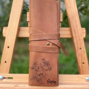 May include: A brown leather pencil case with a floral design and the name "Sophy" engraved on it.