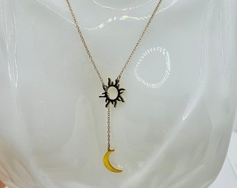 May include: A gold chain necklace with a sun and moon pendant. The sun pendant is a stylized sun with a circle in the center. The moon pendant is a crescent moon.