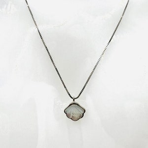 Könnte beinhalten: Eine silberne Kettenkette mit einem weißen Muschel Anhänger.