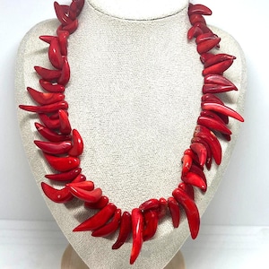May include: A vibrant red necklace displayed on a mannequin. The necklace is composed of numerous, irregularly shaped, polished red pieces, creating a bold and eye-catching accessory. The necklace is a statement piece, perfect for adding a pop of color.