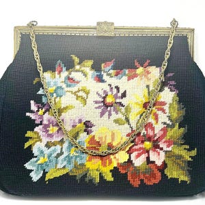Könnte beinhalten: Schwarze Handtasche mit floralem Gobelindesign. Die Tasche hat einen goldfarbenen Metallrahmen und einen Kettenriemen. Das Gobelindesign zeigt einen Strauß bunter Blumen in Rot-, Gelb-, Lila- und Blautönen.