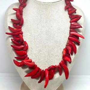 May include: A vibrant red necklace displayed on a mannequin. The necklace is composed of numerous, irregularly shaped, polished red pieces, creating a bold and eye-catching accessory. The necklace is a statement piece, perfect for adding a pop of color.
