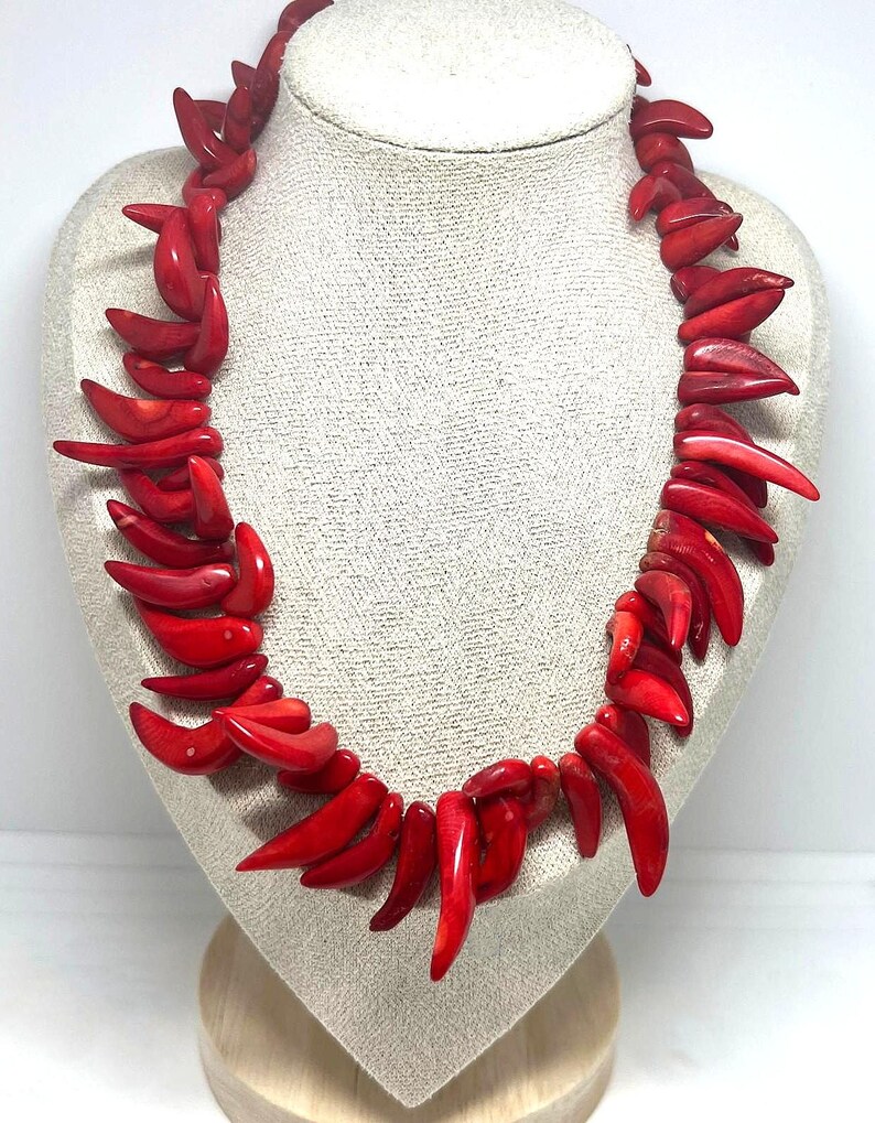 May include: A vibrant red necklace displayed on a mannequin. The necklace is composed of numerous, irregularly shaped, polished red pieces, creating a bold and eye-catching accessory. The necklace is a statement piece, perfect for adding a pop of color.