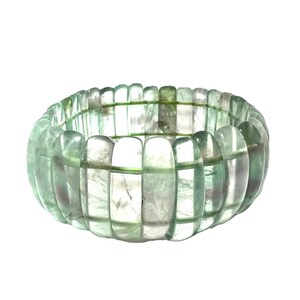 Op de afbeelding: Een lichtgroene armband met een geribbeld ontwerp. De armband is gemaakt van doorschijnende, rechthoekige kralen die aan elkaar zijn geregen. De kralen hebben een subtiele, gemarmerde uitstraling, met hints van paars en groen.