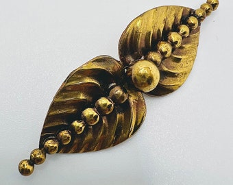 Könnte beinhalten: Eine goldfarbene Brosche mit einem Blattdesign und einer Reihe runder Perlen. Die Brosche ist aus Metall und hat eine strukturierte Oberfläche.