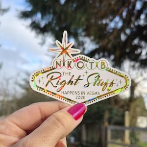 May include: A holographic sticker in the shape of the Las Vegas sign. The sticker reads "NKOTB The Right Stuff HAPPENS IN VEGAS 2026" with a starburst design at the top. The sticker has a white border with gold accents.