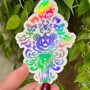 May include: A rainbow iridescent vinyl sticker featuring the Haunted Mansion's iconic wallpaper pattern with Mickey Mouse's head in the center. The sticker features a spider, bats, and ghosts.