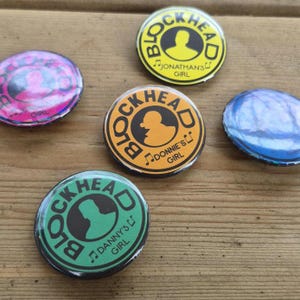 May include: A collection of round pinback buttons with the word "BLOCKHEAD" in a circular design. The buttons feature various color schemes, including yellow, orange, and green, with silhouettes and musical notes. Some buttons have text like "JONATHAN'S GIRL" and "DONNIE'S GIRL".