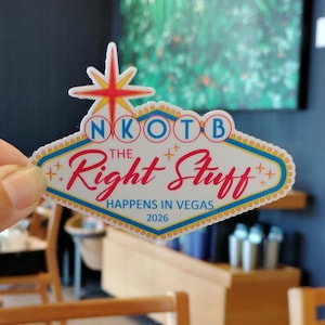 Op de afbeelding: Een sticker in de vorm van het iconische Las Vegas-bord, met de tekst "NKOTB The Right Stuff HAPPENS IN VEGAS 2026." Het bord heeft een witte achtergrond met rode, blauwe en gele accenten en een sterrenpatroon.