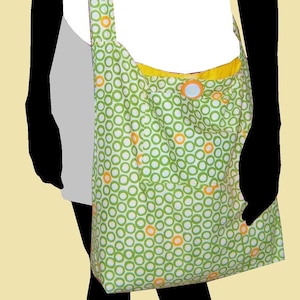 May include: A green and white fabric tote bag with a yellow and orange circle pattern. The bag has a single strap and a button closure.