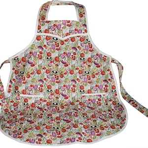 May include: A white apron with a colorful vegetable print. The apron has two pockets and a white trim.