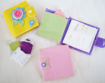 May include: Three small felt sewing kits in different colours and designs. The kits include needles, thread, and a small flower embellishment.
