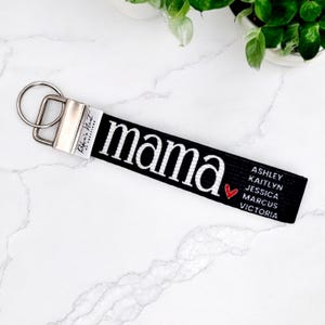 Peut inclure: Porte-clés noir avec le mot "mama" en blanc, un cœur rouge et les noms : Ashley, Kaitlyn, Jessica, Marcus et Victoria. Il possède un fermoir et un anneau en métal argenté.