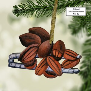 May include: A hand-painted wooden Christmas ornament depicting a cluster of pecans. The ornament is two-sided and features a brown and red color scheme. The text "2 Sided 2D Flat Ornament Not 3D" is printed on the ornament.