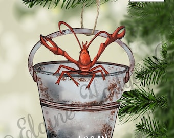 May include: A red lobster in a rusty metal bucket with the name "LOGAN" written on the side. The ornament is two-sided and flat, not 3D.