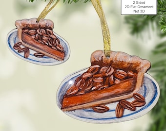 May include: A two-sided, flat wooden ornament depicting a slice of pecan pie on a white plate with blue trim. The ornament is decorated with a watercolor-style painting of the pie and pecans. The ornament is labeled "2 Sided 2D Flat Ornament Not 3D".