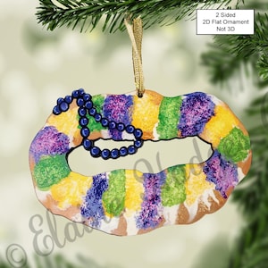 May include: A two-sided, flat, wooden ornament shaped like a King Cake with purple, green, and gold icing and a string of blue beads. The ornament is not 3D. The text "2 Sided 2D Flat Ornament Not 3D" is printed on the ornament.