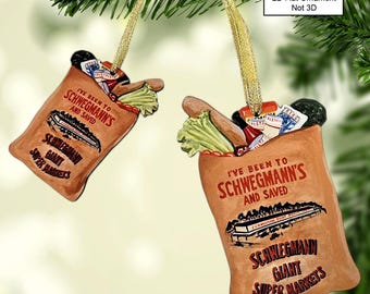 Könnte beinhalten: Zweiseitiger Weihnachtsbaumschmuck mit einer braunen Papiertüte mit dem Text "Ich war bei Schwegmann's und habe gespart" und dem Schwegmann Giant Super Markets Logo. Die Tüte ist gefüllt mit Lebensmitteln, darunter ein Brot, ein Salatkopf, eine Ketchupflasche und ein Gurkenglas.