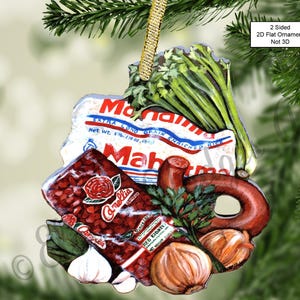 May include: A Christmas ornament featuring a red and white can of beans, a brown sausage, a bunch of green celery, a white onion, and a bag of rice. The bag of rice has the text "EXTRA LONG GRAIN ENRICHED RICE" and "Net Wt. 1 lb (16 oz. 454g)". The can of beans has the text "Camellia" and "RED KIDNEYS". The ornament is two-sided and flat, not 3D.