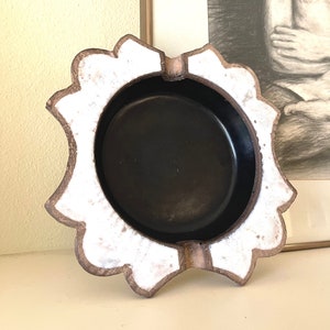 May include: A white and brown ceramic ashtray with a scalloped edge and a black interior.