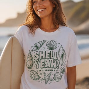 Könnte beinhalten: Ein weißes Kurzarm-T-Shirt mit einem dunkelgrünen Grafikdruck verschiedener Muscheln und eines Seesterns, die in einem Kreis angeordnet sind. In der Mitte des Designs steht der Text "SHELL YEAH!" in Fettdruck mit "IT'S SUMMER" darunter.