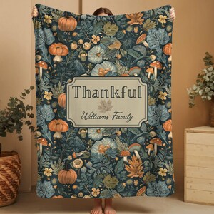 Könnte beinhalten: Eine dunkelblaue Decke mit einem Blumen- und Kürbismuster. Die Decke trägt den Text "Thankful Williams Family" in einem dekorativen Rahmen. Das Design umfasst orangefarbene Kürbisse, Pilze und verschiedene Blätter.