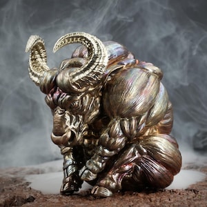 May include: A detailed, metallic sculpture of a bull with gold horns. The sculpture is sitting on a textured surface and is surrounded by smoke.