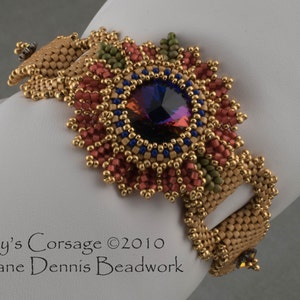 May include: A gold, red, and green beaded bracelet with a large purple gemstone in the center. The bracelet has a clasp and is decorated with a floral design. "Sky's Corsage ©2010 Diane Dennis Beadwork" is written below the bracelet.