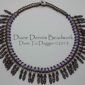 May include: A purple and silver beaded necklace with a fringe of purple and gold beads. The necklace is made with square and teardrop-shaped beads. The text "Diane Dennis Beadwork Dare To Dagger ©2013" is visible in the center of the image.