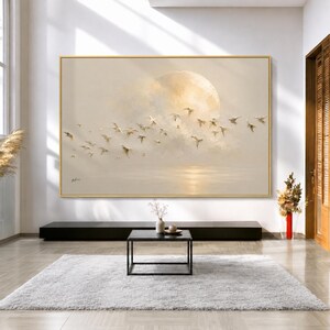 Könnte beinhalten: Ein großes rechteckiges Wandbild in einem goldenen Rahmen mit einem Ölgemälde, das einen Vogelschwarm zeigt, der über einen weichen, cremefarbenen Himmel mit einem großen, leuchtenden Mond und einem ruhigen, reflektierenden Gewässer fliegt.