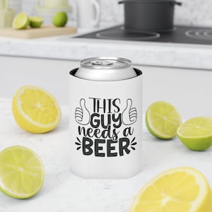 May include: A white cylindrical can cooler featuring black text that reads THIS GUY needs a BEER, accompanied by two thumbs-up icons on either side of the text. The can cooler is positioned upright and holds a silver aluminum beverage can.