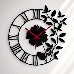 May include: Black wall clock with Roman numerals, a floral center, and red hands. Decorative leaves and vines frame the clock face. The clock is a stylish home decor item.