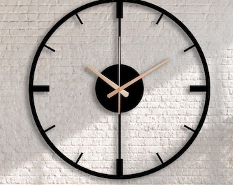 May include: A large, circular wall clock featuring a black metal frame with thin, minimalist hour markers and a central black disc. The clock has two slender, metallic gold hands positioned against the white brick wall background.