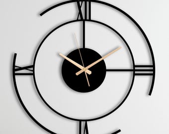 May include: A large, circular wall clock featuring a black metal frame with an open, skeletal design. It displays Roman numerals at the twelve, three, six, and nine o'clock positions. The center has a solid black disc with thin, gold-colored hands.