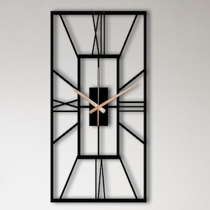 May include: A rectangular wall clock featuring a black metal frame with an open geometric design and Roman numerals. The clock has a central black rectangular block with two thin, light-colored hands indicating the time against the wall.
