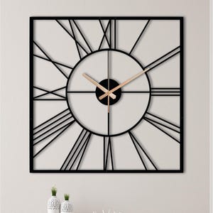 Peut inclure: Une horloge murale carrée dotée d'un cadre en métal noir avec de fines lignes rayonnantes partant d'un cadran circulaire central. Les aiguilles de l'horloge sont de couleur or rose métallique, contrastant avec la structure géométrique noire.